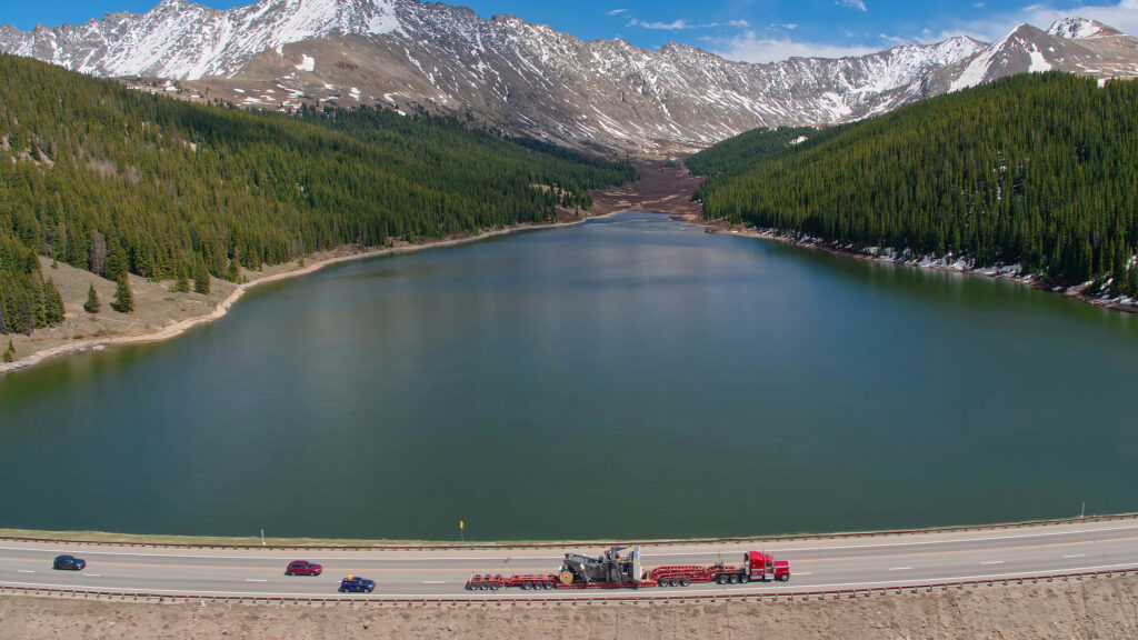 Transporting industrial heavy equipment with flatbed trucks next to lagoons and forests in British Columbia, Canada.